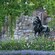 A statue of a man on a horse near flowers, trees and a wall